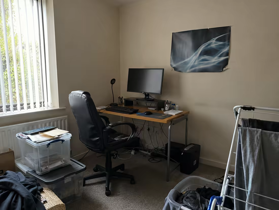 A cramped home office corner with tangled cables and storage boxes