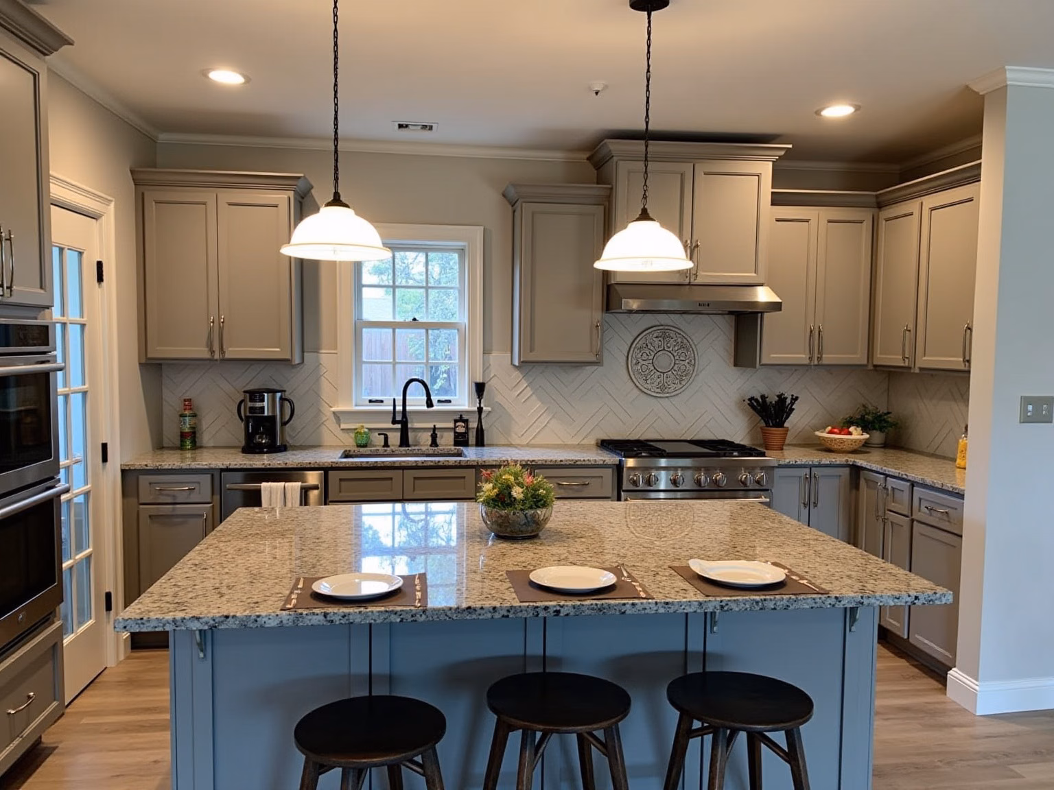 The kitchen as another tool made it: grey cabinets, a window over the sink, a glass door on the left, a range with a hood, a granite island with three stools and recessed spotlights instead of the track lights